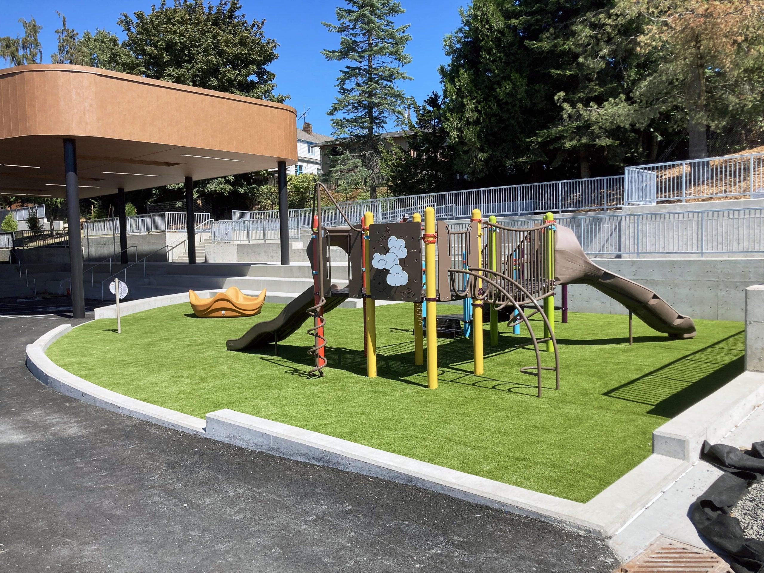 playground equipment sites on a green surfaced area with curbing around it. 它后面有一座建筑